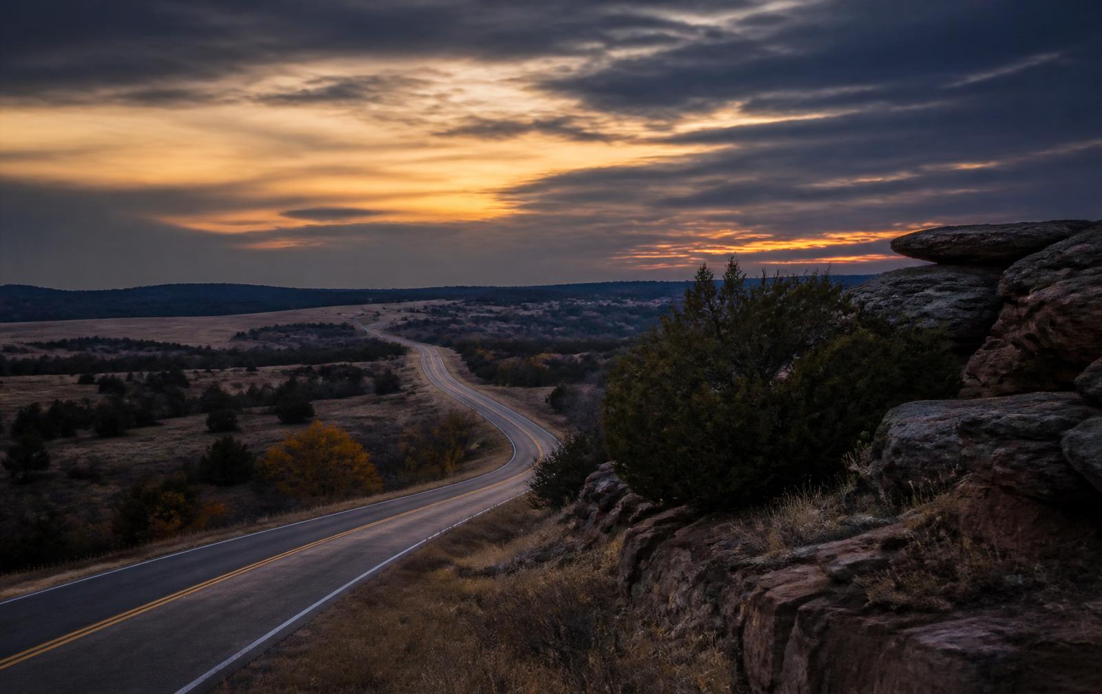 Two-lane highway curving through northeastern Oklahoma prairie and sandstone at dusk